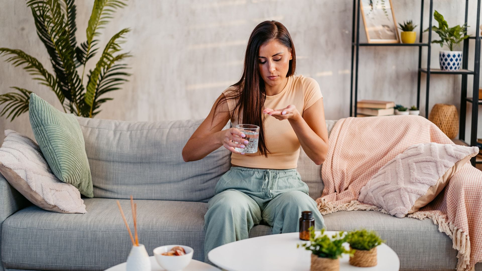 mujer joven tomando unas pastillas sentada en el sofá