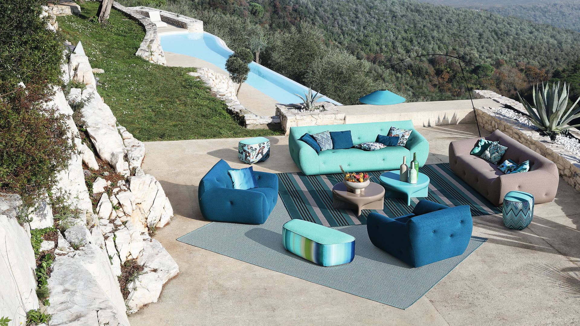Salón exterior en una terraza en una casa de montaña, al lado de la piscina con sofás y pufs en azul 
