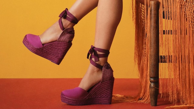 Piernas de mujer sentada en una silla con mantón naranja y alpargatas de cuña rosas