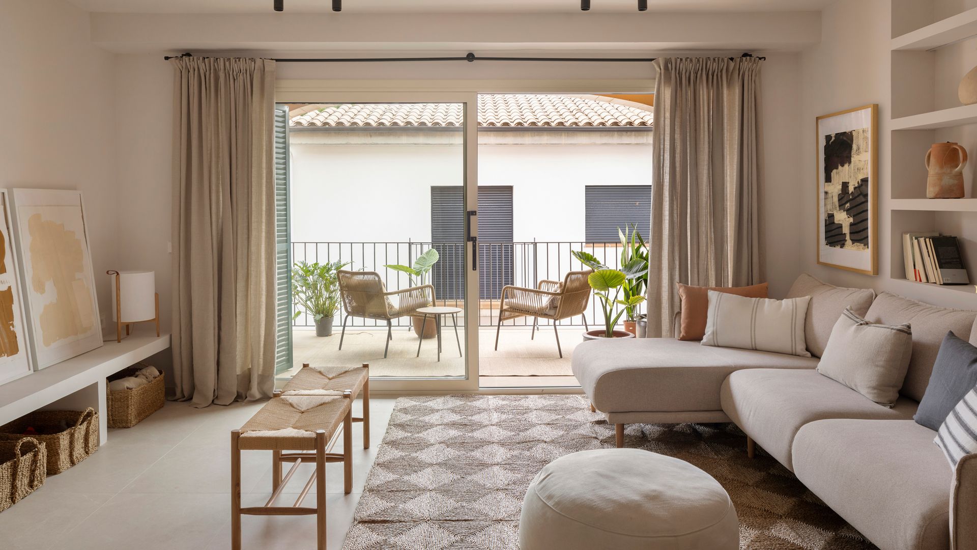 Salón con alfombra de yute, estantería de obra, banquetas de mimbre, salida al jardín, sofá beige, puff, cestos