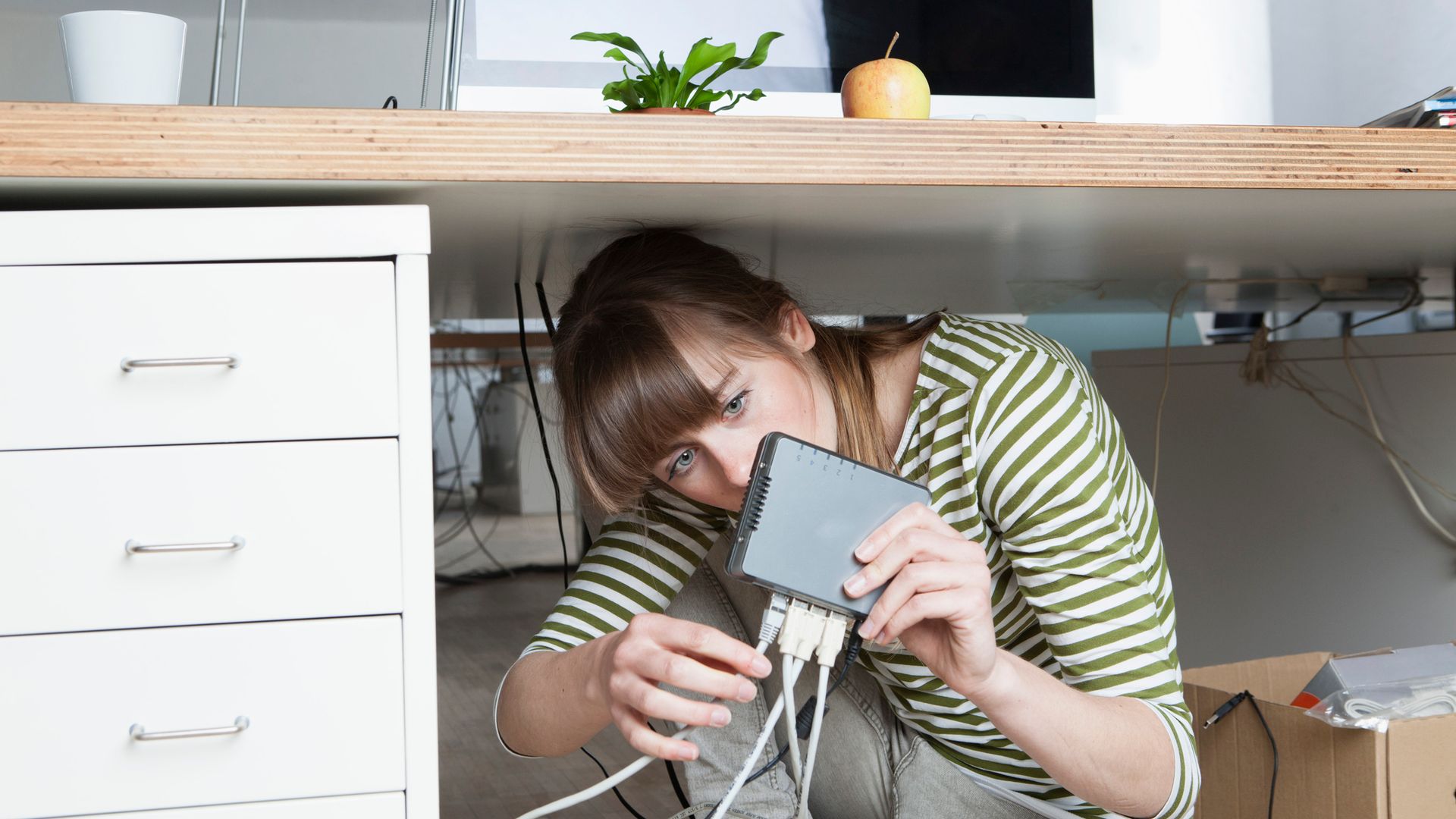 Mujer comprobando el router debajo de la mesa 