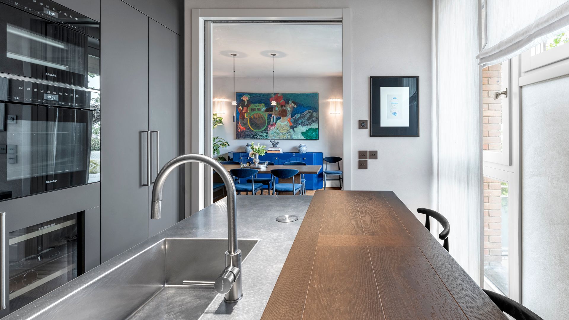 Cocina que comunica con el comedor mediante corredera blanca, muebles hasta el techo en gris oscuro, hornos y microonda en columna, isla de madera y acero