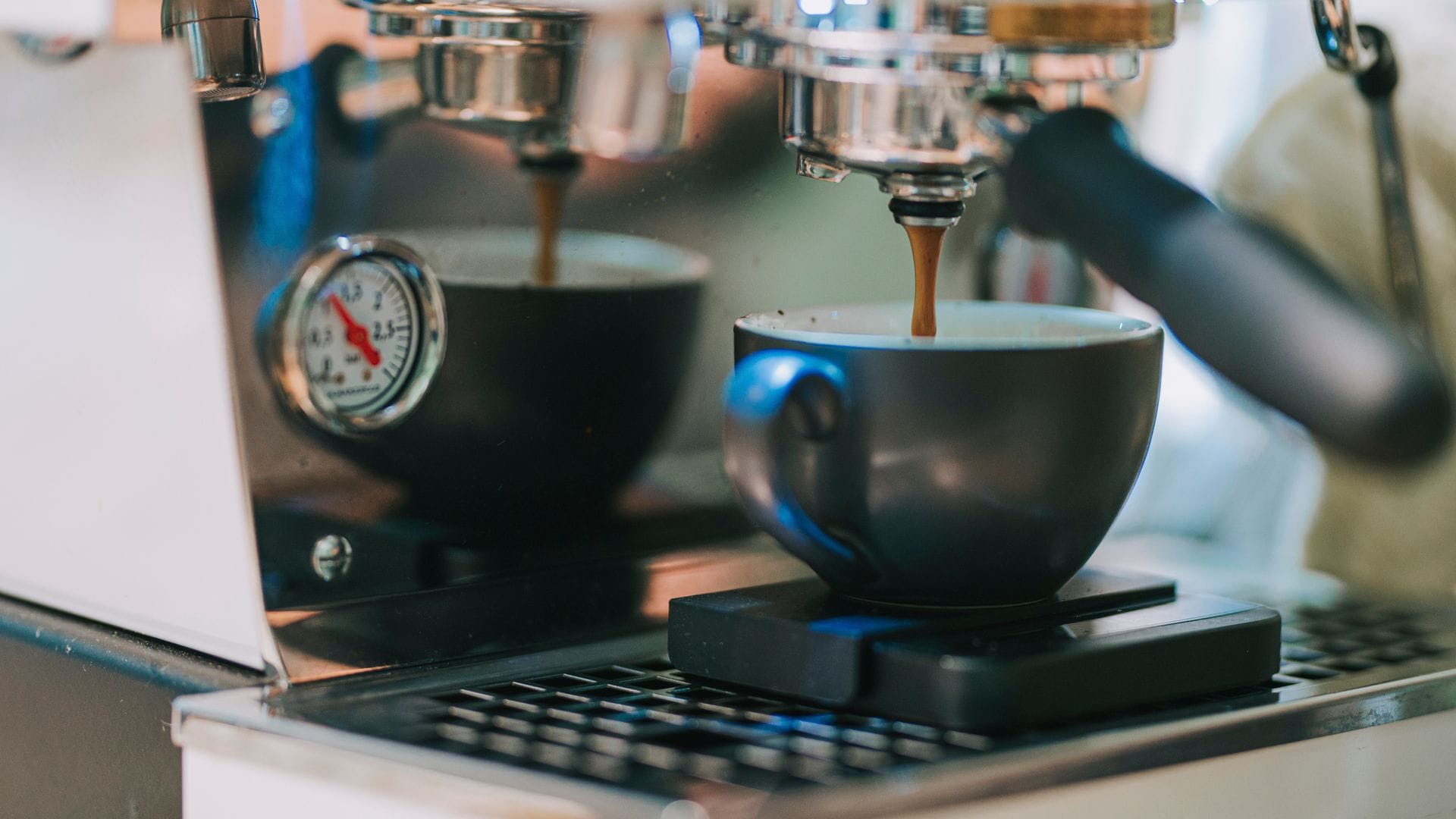 Cafetera con molinillo en un plano detalle con taza de café en primer plano y el café cayendo poco a poco.