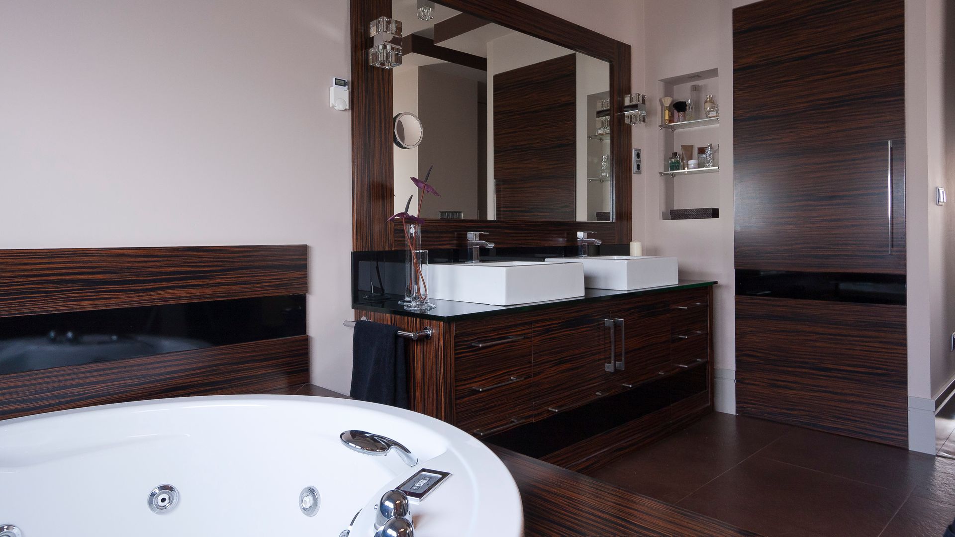 Baño con bañera exenta, mueble bajolavabo oscuro, puerta a juego, espejo con marco de madera oscura, lavabos sobre la encimera, hornacina