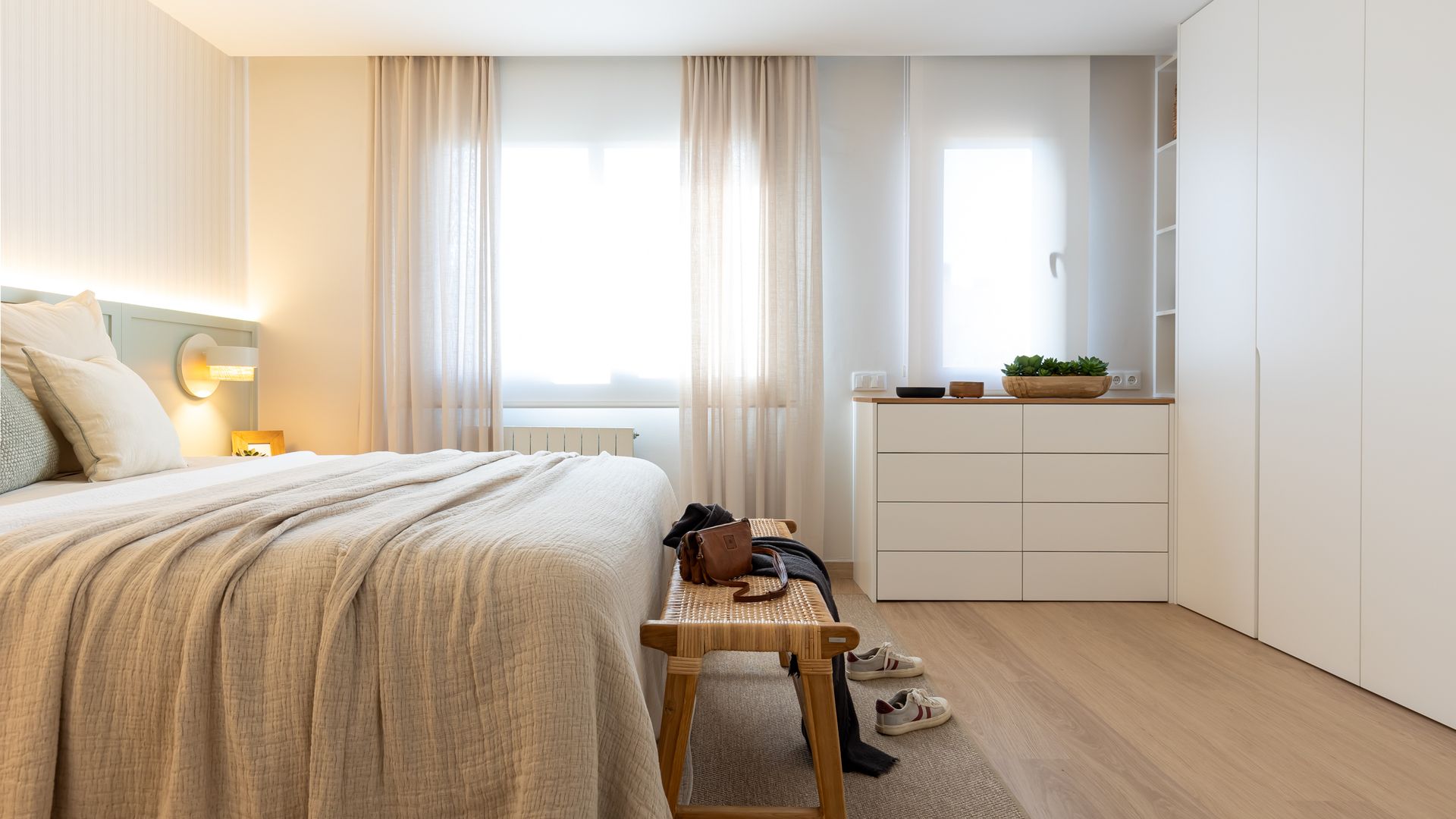 Dormitorio con cortinas beige hasta el suelo, ropa de cama beige, cando de fibras vegetales, alfombra de fibras vegetales, cómoda y armario blancos 