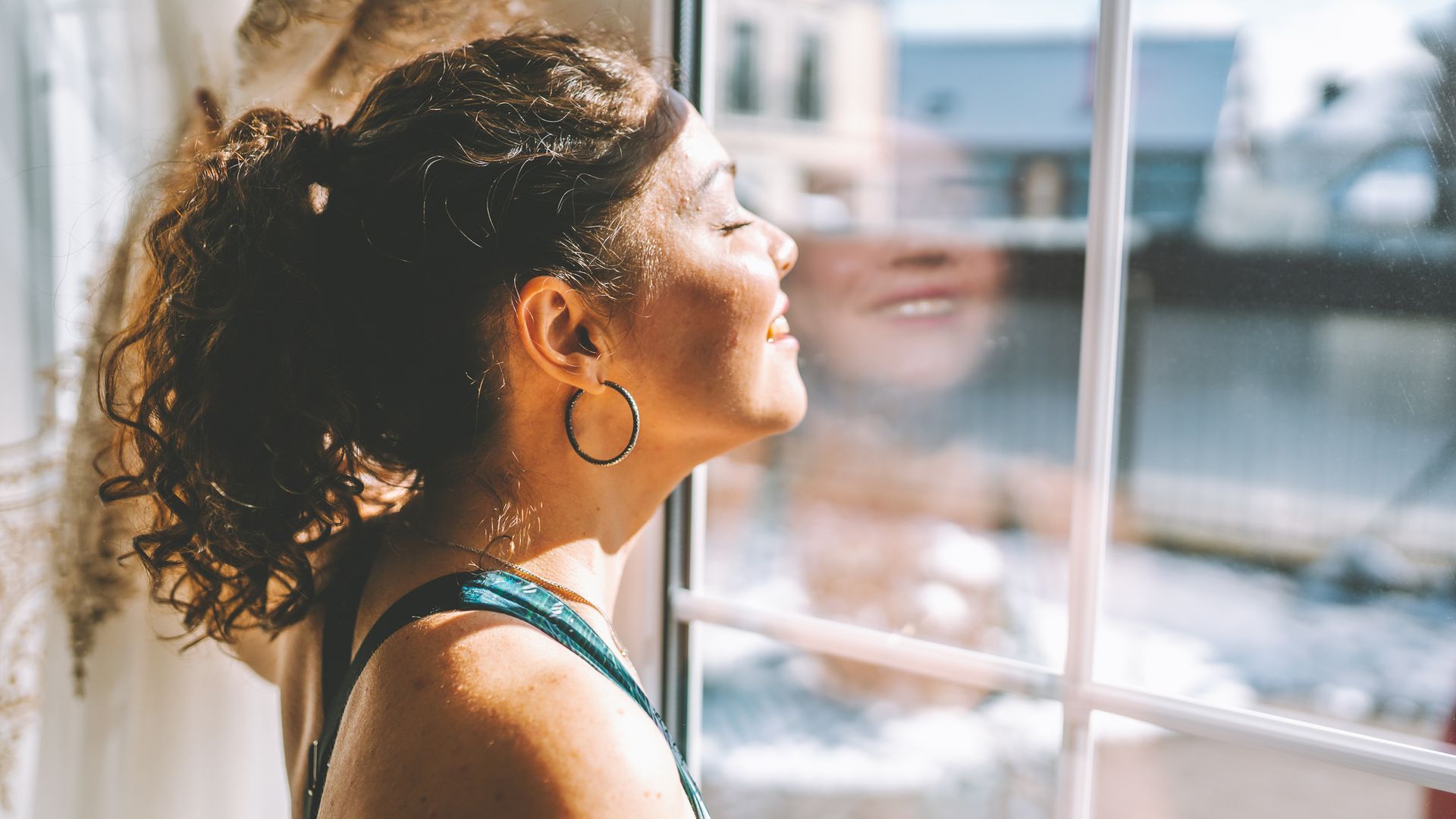mujer joven mirando por la ventana mientras le da el sol en el rostro