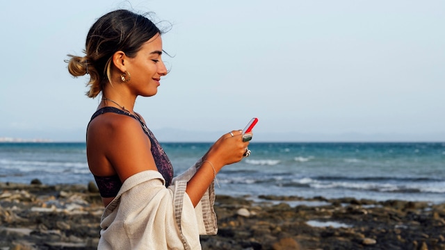 mujer sonriente usando el móvil en la playa