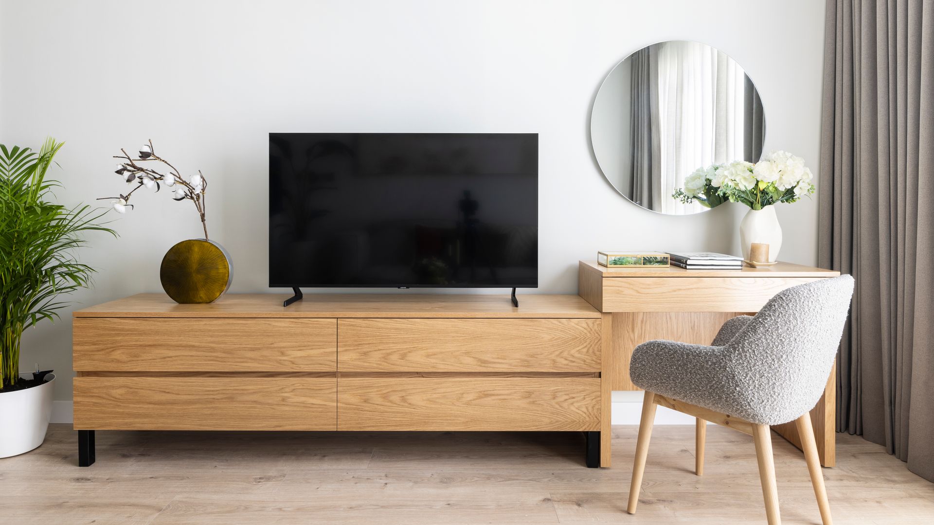 Mueble de televisión de madera, junto a rincón tocador con espejo redondo, silla tapizada