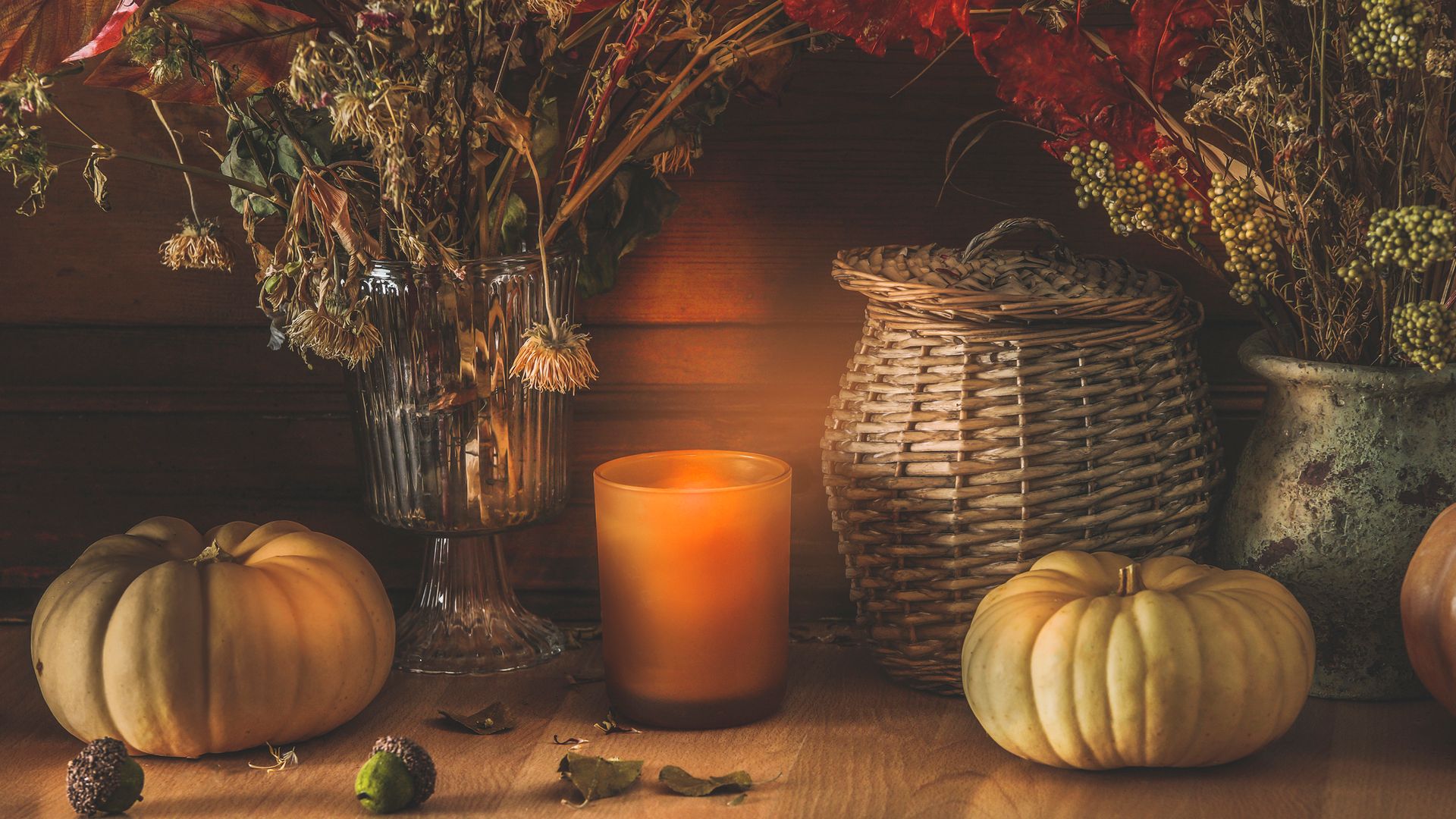 Mesa decorada para el otoño con calabazas, velas en naranja, cestas y jarrones con diferentes tipos de flores secas.