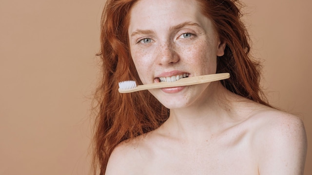 Mujer pelirroja con el cepillo de dientes en la boca