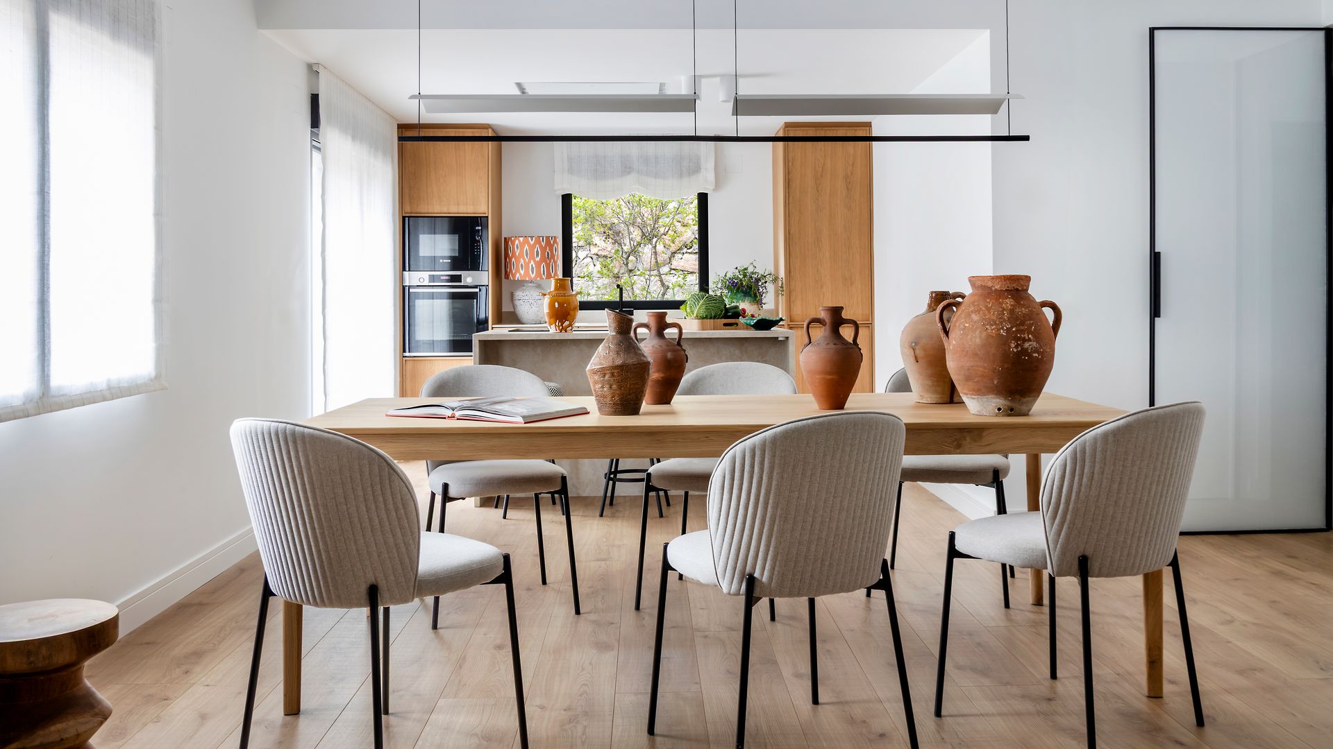 Cocina con comedor con mesa de madera, sillas blancas, lámparas de techo 