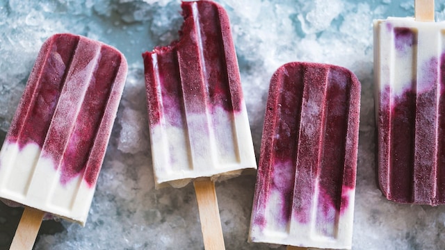 Helados en formato polo de frutas del bosque y yogur, sobre una superficie helada.
