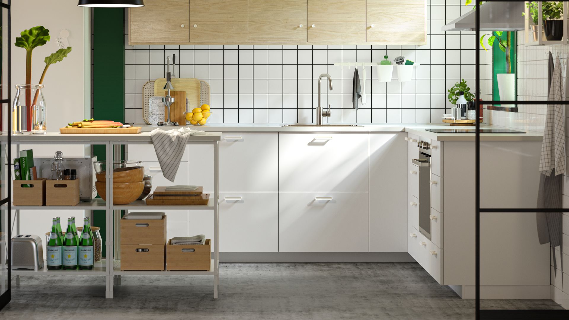 Cocina IKEA con muebles blancos, azulejos de cuadros, armarios de madera, mesa abierta con cajas y botellas, lámpara de techo negra