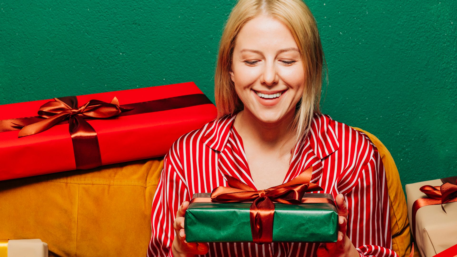 Mujer rubia con pijama camisero de rayas sentada en un sofá rodeada de regalos
