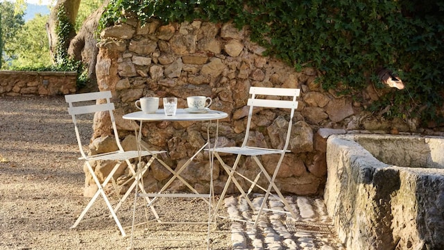 Jardín exterior con una pequeña mesa en blanco de hierro y dos sillas con el atardecer de Maisons du Monde