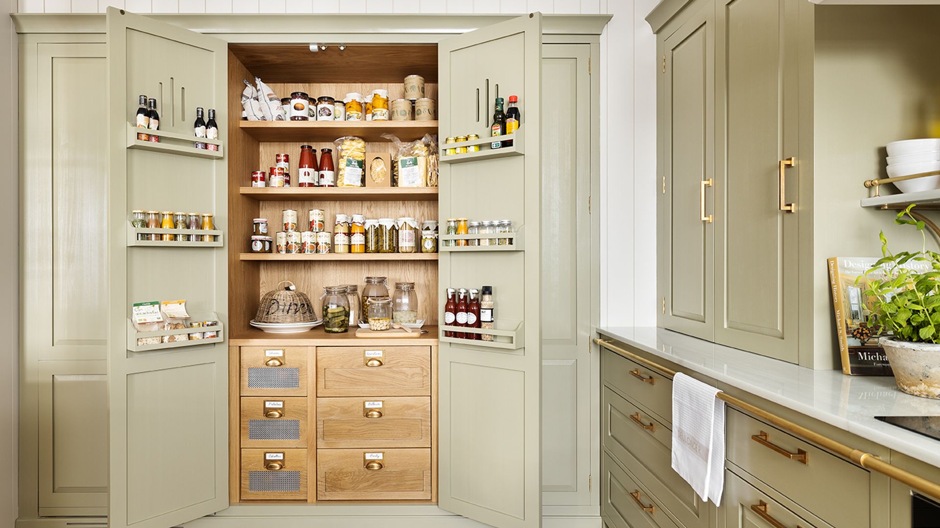 Cocina en color verde claro con despensa abierta con cajones y baldas de madera, estantes en sus puertas, suelo de madera