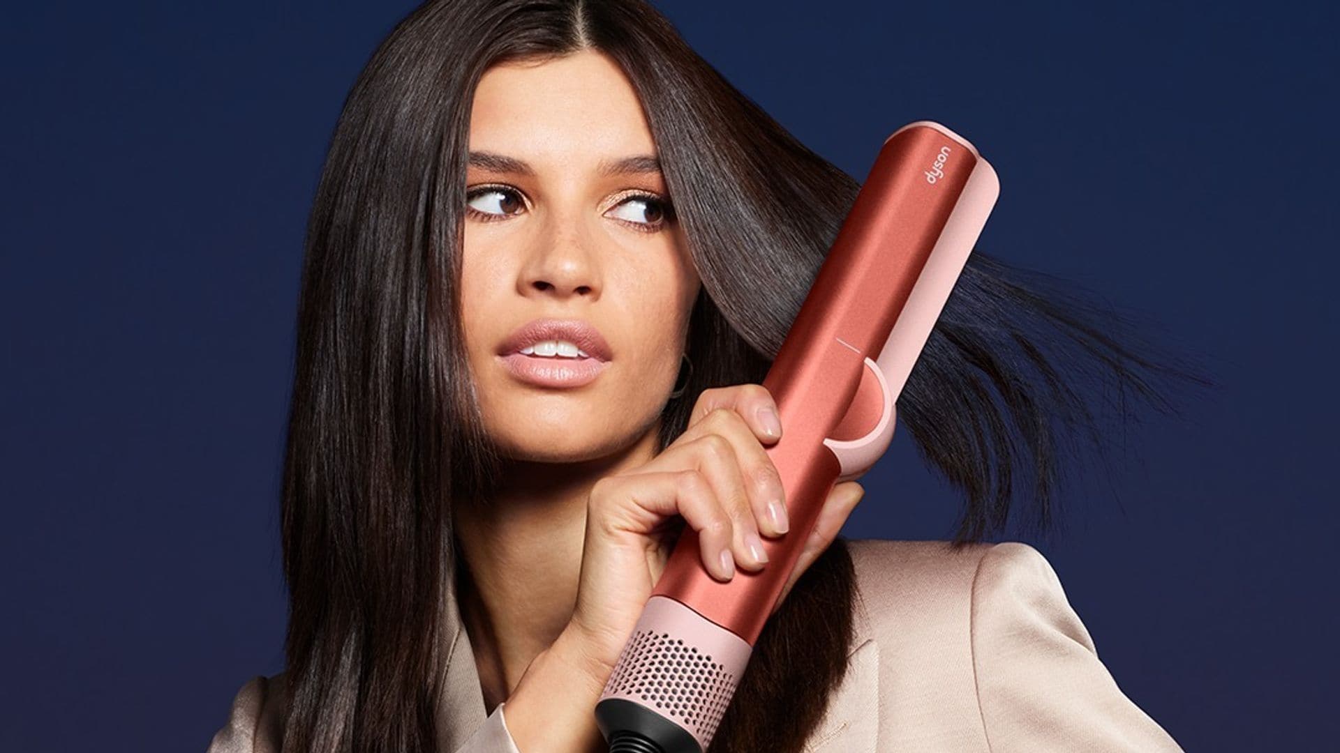 Mujer con traje satinado rosa claro alisándose el pelo moreno con plancha de pelo Airstrait de Dyson
