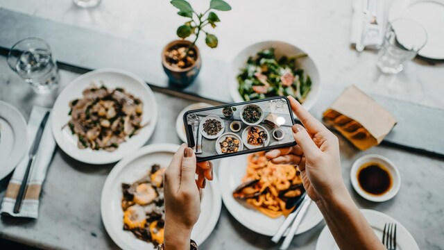overhead view of a woman 39 s hand taking photo of freshly served food before eating it with smartphone in a restaurant