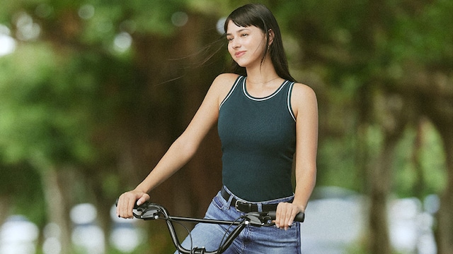 Mujer joven montando en bicicleta con vaqueros y top de Uniqlo