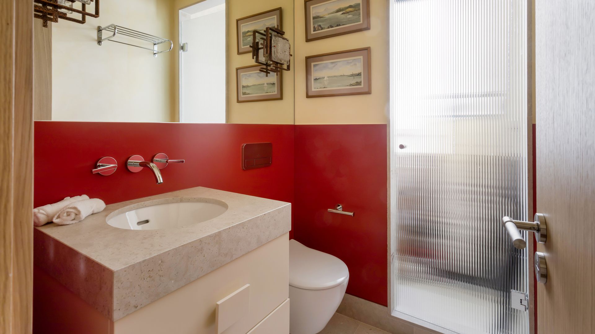 Baño con zócalo rojo, espejo de pared a pared, encimera de piedra, apliques de pared