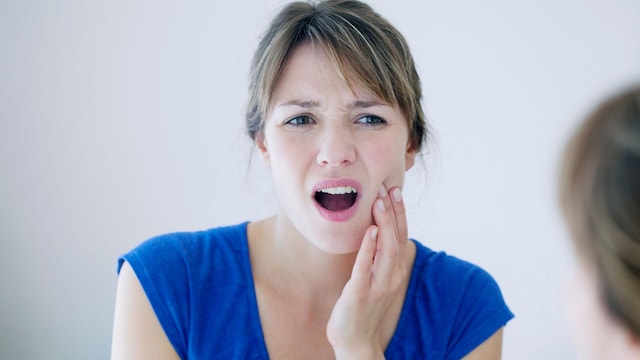 mujer con dolor en la boca mirándose al espejo