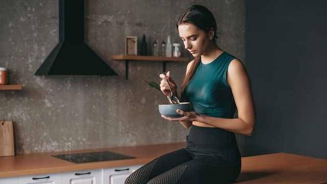 mujer joven con ropa deportiva comiendo sentada en la encimera de la cocina