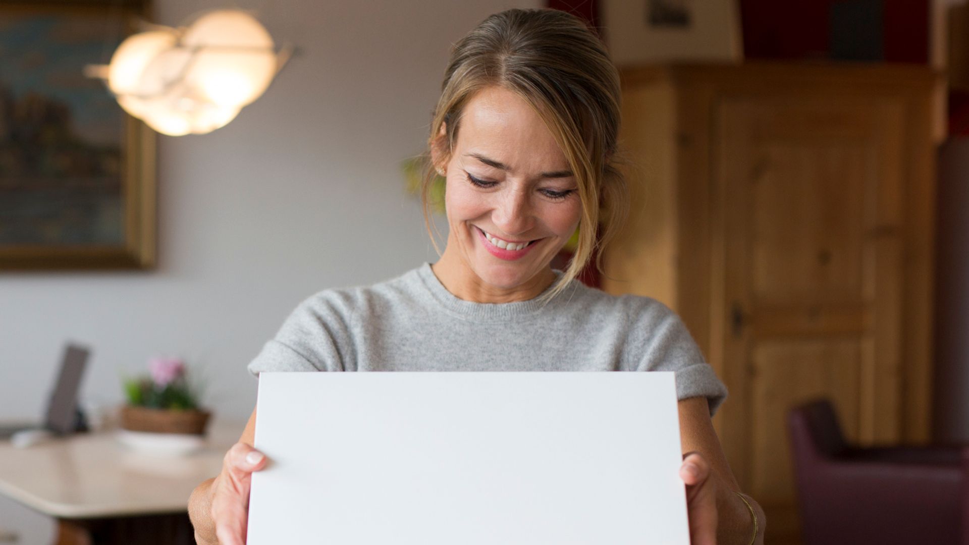 Mujer madura abriendo sonriente una caja en el interior de su salón