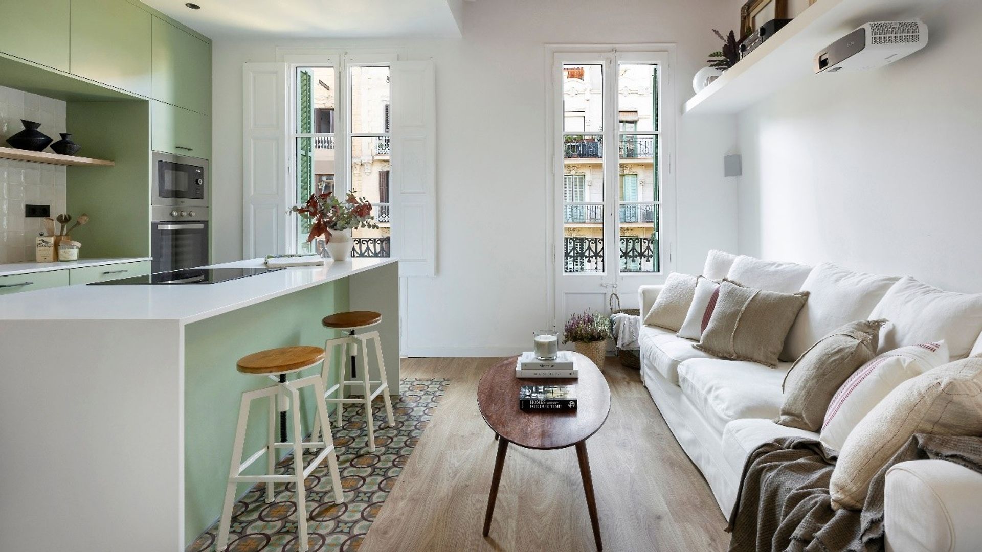 Cocina abierta al salón, con grandes ventanales con salida al balcón, muebles verdes hasta el techo, sofá blanco, suelo hidráulico, cocina con isla, bóveda catalana 