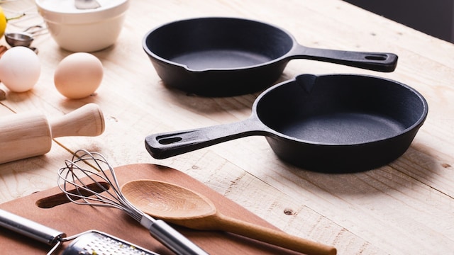 Sartenes de hierro fundido encima de una mesa con accesorios de cocina como un rodillo, una cucharada de palo y medidores