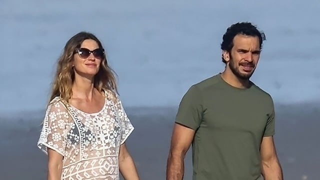 La pareja pasea junto a la orilla del mar. Para la ocasión, ella apostó por un bikini negro y un minivestido blanco de encaje y transparencias