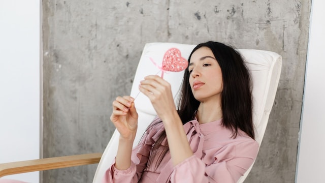 mujer melancólica mirando un corazón, sentada en una silla