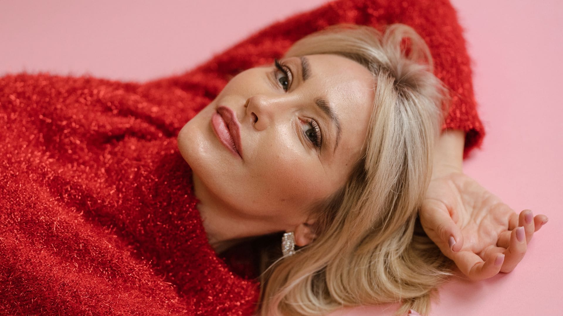 Mujer madura tumbada en el suelo con jersey rojo de fiesta y piel jugosa y luminosa