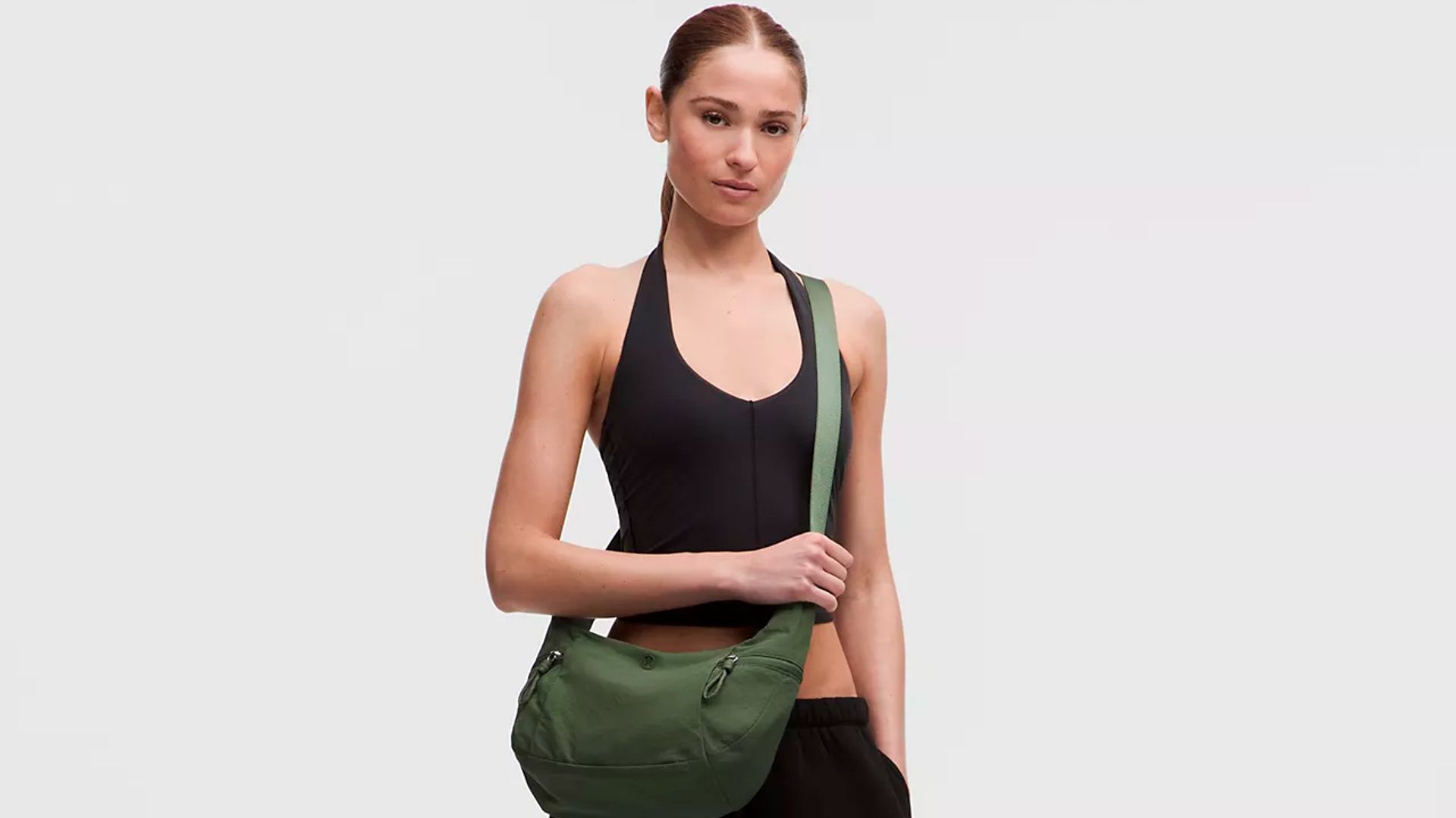 Mujer joven pelirroja con conjunto de deporte negro y bolso de hombro verde de Lululemon