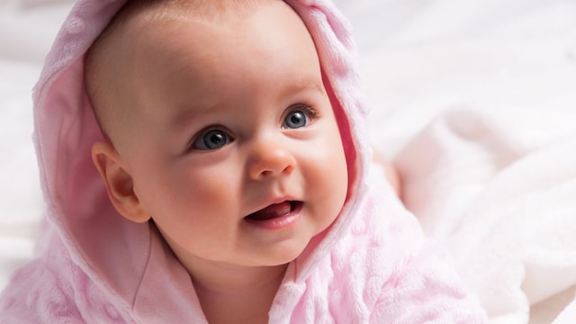 Bebé niña con rostro dulce y ojos claros lleva albornoz rosa