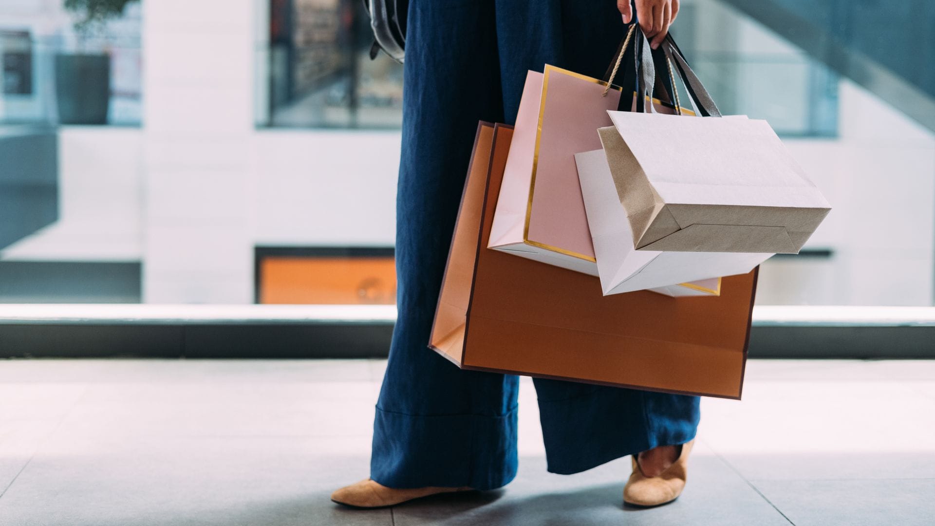 Mujer con bolsas de la compra en un centro comercial, se le ve desde la cadera hasta los pies, con ropa de otoño-invierno.