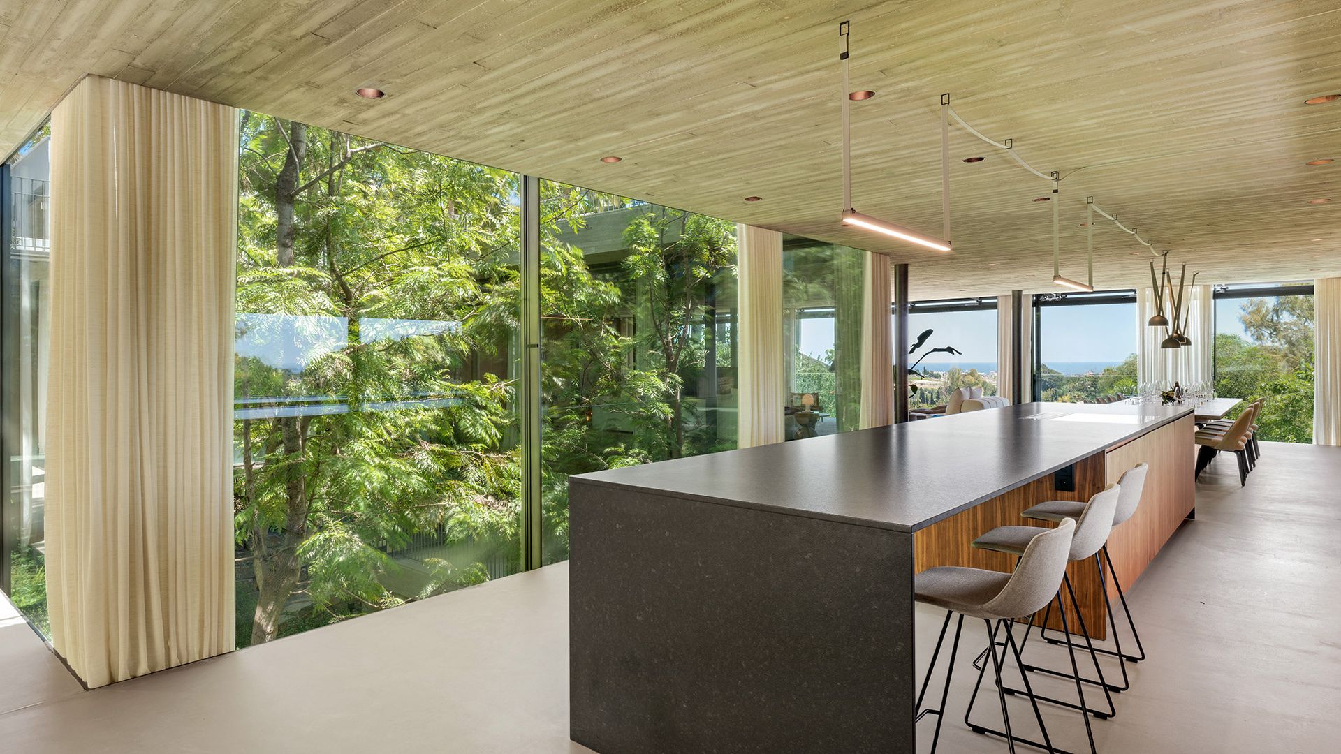 Isla de cocina con zona de barra con taburetes alto, lámparas de techo, tabiques de cristal, techo de hormigón y cortinas beiges