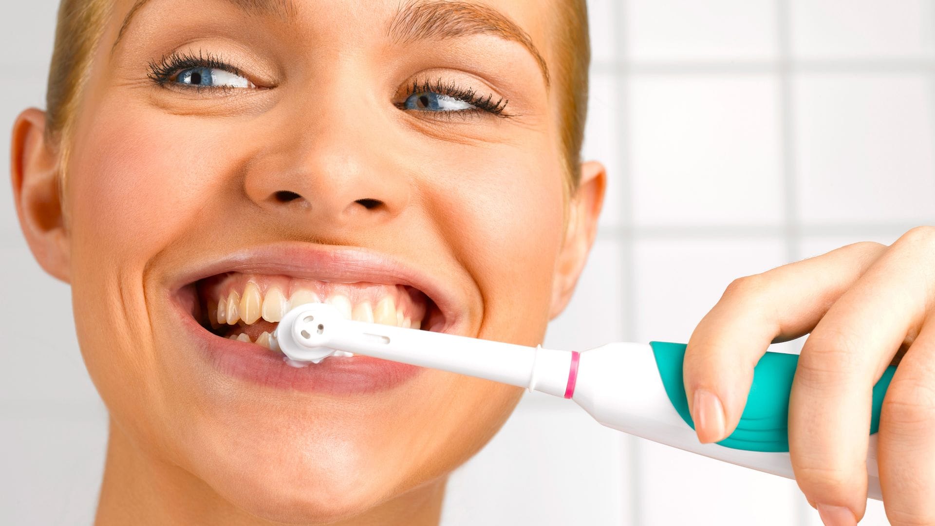 Mujer lavándose los dientes con un cepillo de dientes eléctrico en primer plano.