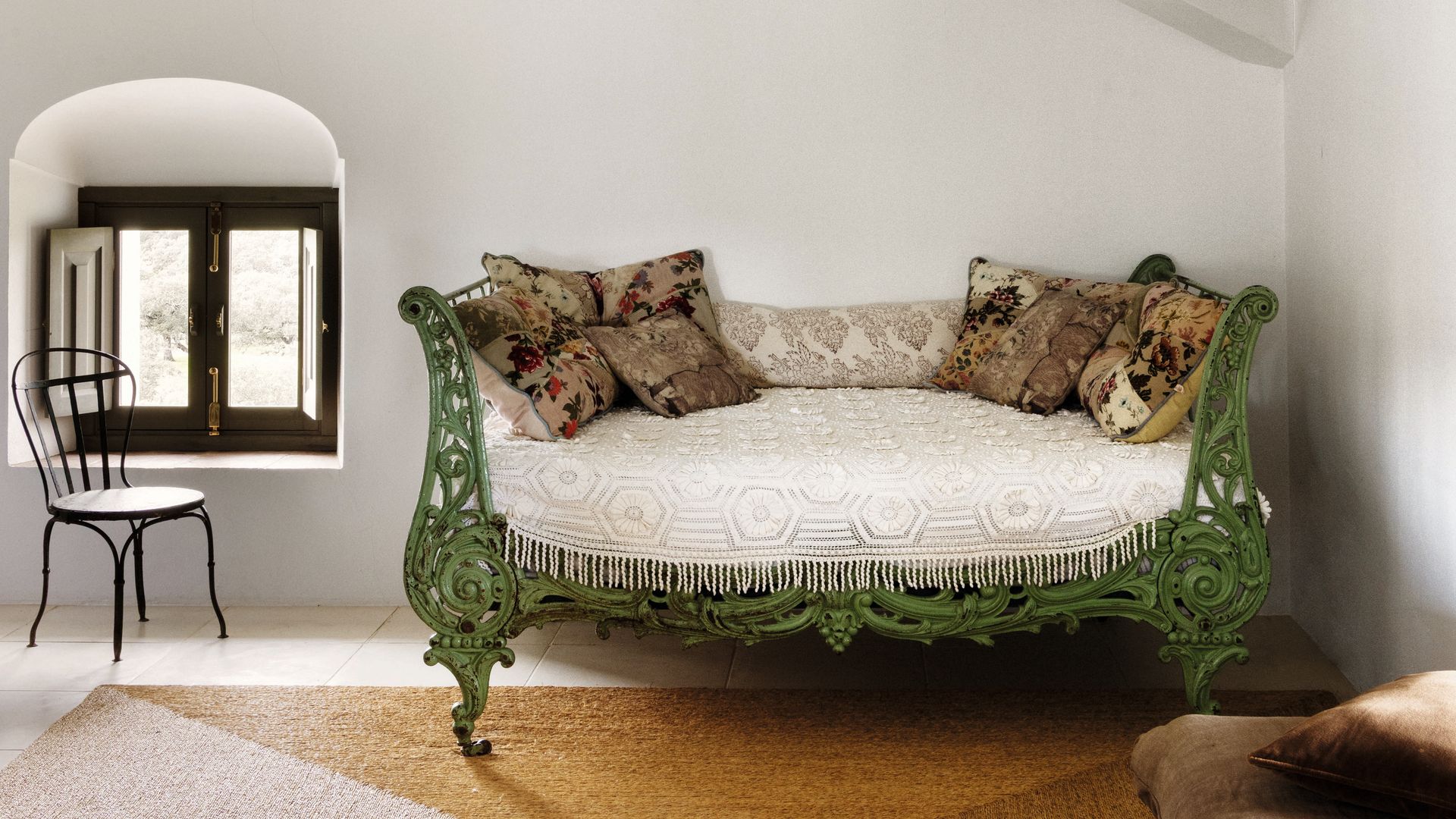 Habitación con sofá verde antiguo, varias almohadas, silla y ventana.