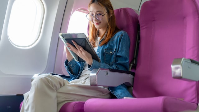 Una mujer en un avión sentada con una tablet en sus manos