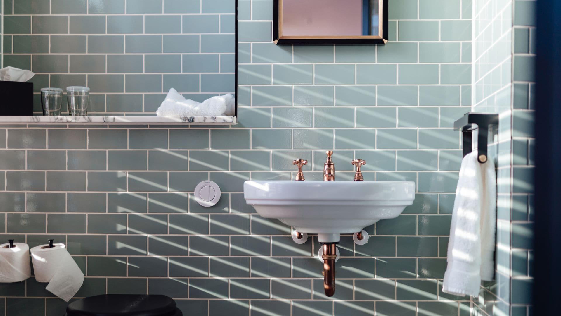 Decoración de baño interior en verde, blanco y negro, con una foto en detalle del lavabo, el WC, el toallero y un espejo grande.