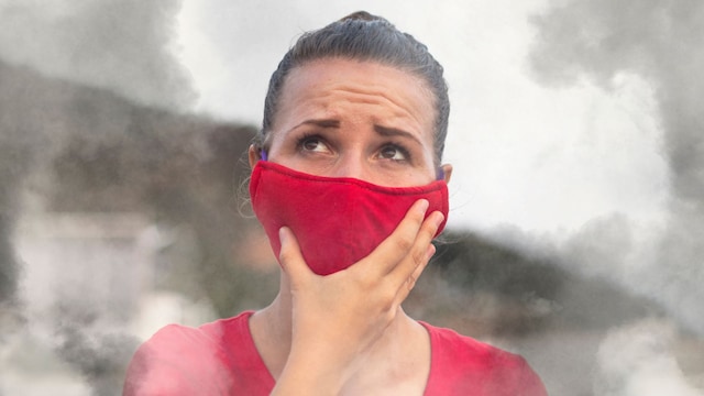 Mujer protegiéndose con una mascarilla de color rojo del humo de un incendio forestal