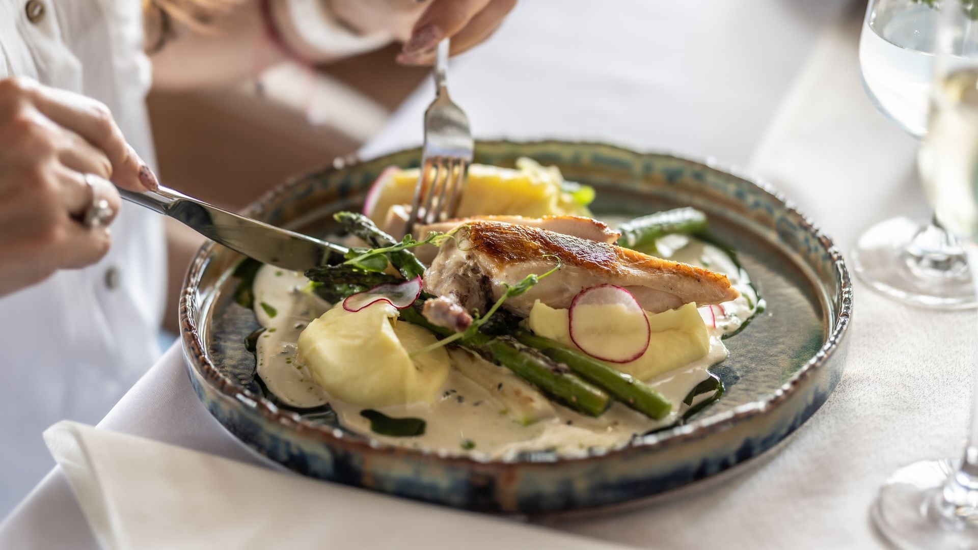 Una mujer cenando un pollo a la plancha con patatas y espárragos