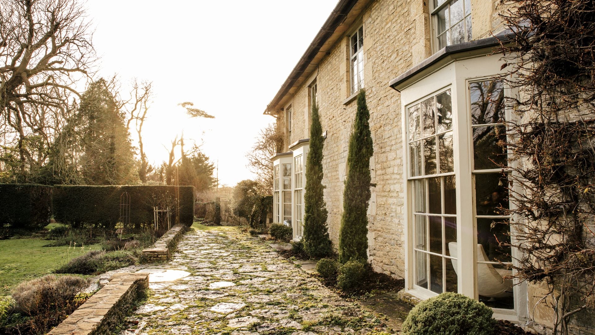 Camino de piedra frente a una casa de campo con ventanas grandes