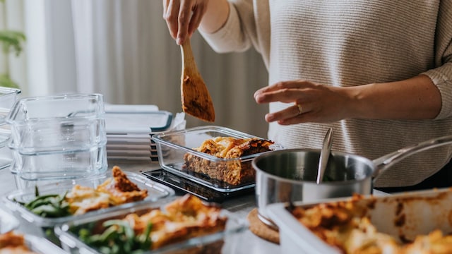 Mujer pesando táperes con comida en la encimera de su cocina.