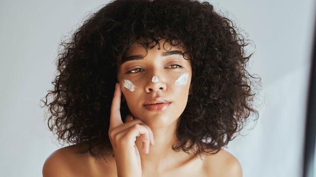 Mujer morena aplicándose crema hidratante en el rostro