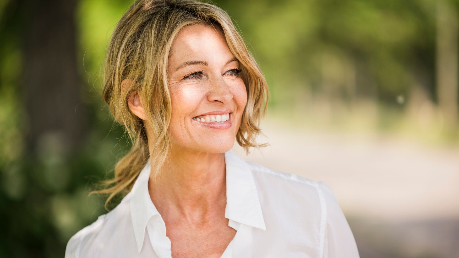 Rostro de mujer madura sonriente con pelo rubio, piel tersa y luminosa, sonriente en la calle