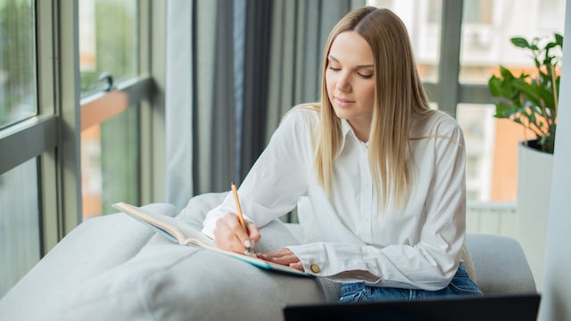 mujer escribiendo en un cuaderno en su casa, junto a una ventana