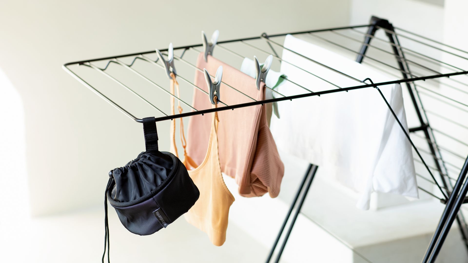 Tendedero metálico negro plegable con ropa y bolsa negra para las pinzas 