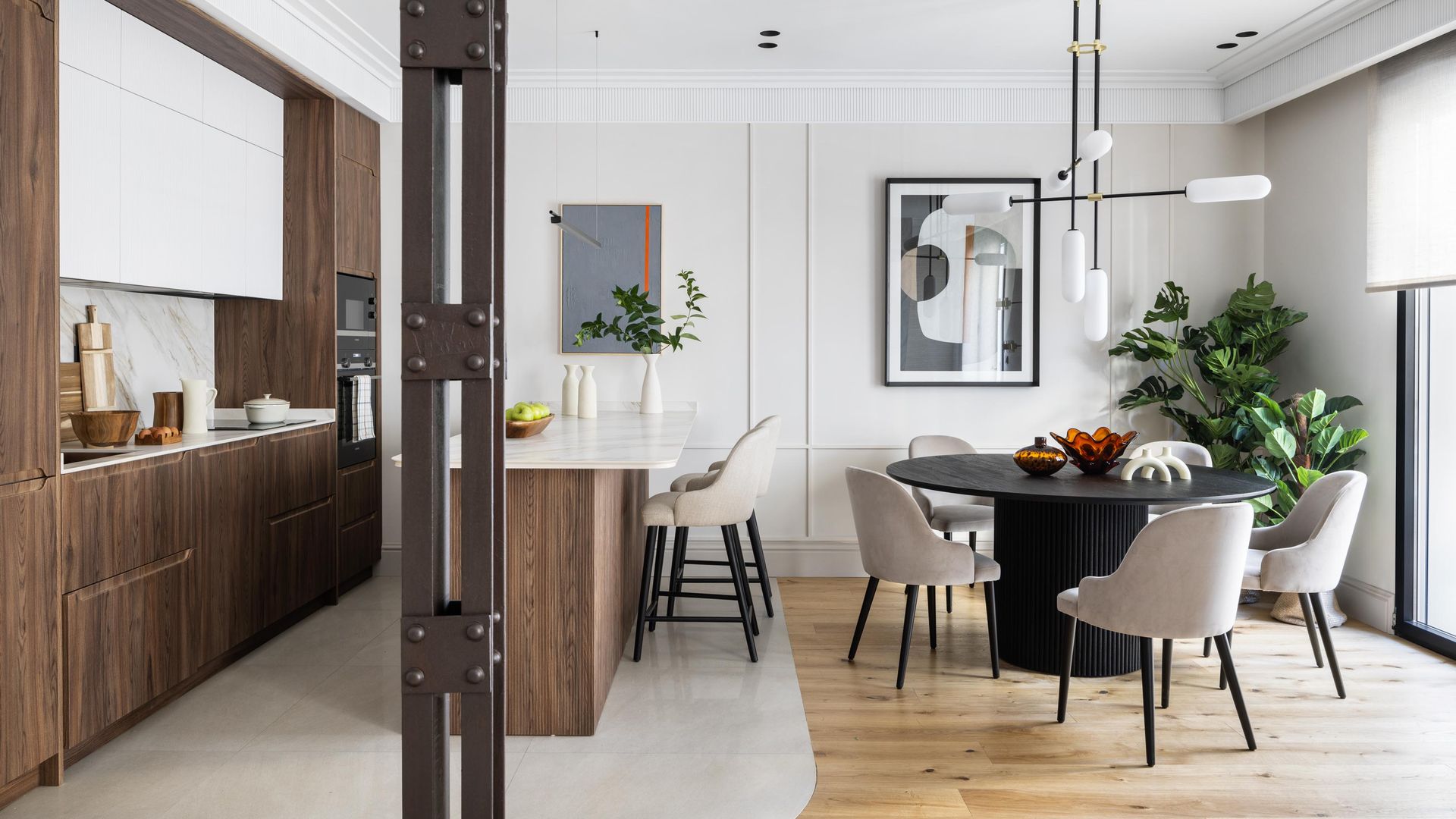 Cocina con comedor con península, muebles de cocina de madera, viga de hierro, suelo de madera en el comedor, lámpara de techo, cuadros