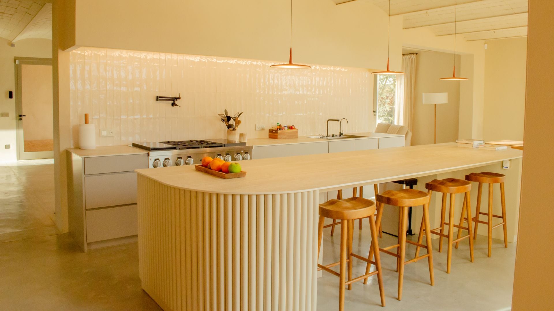 Cocinas con azulejos blancos brillantes, isla de cocina XL, taburetes de madera, bóveda catalana, lámparas de techo